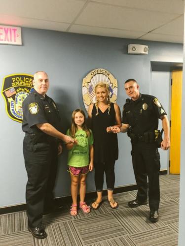 Chief DeMarco and Sgt. Leab presenting a challenge coin to a girl for reporting a child was left unattended in a vehicle. 